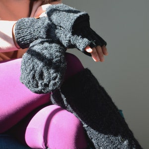 May include: Black knitted fingerless gloves and leg warmers. The gloves have a mitten cover that can be folded back. The leg warmers are long and textured. The person is wearing magenta leggings.