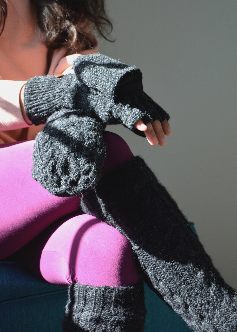 May include: Black knitted fingerless gloves and leg warmers. The gloves have a mitten cover that can be folded back. The leg warmers are long and textured. The person is wearing magenta leggings.