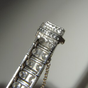 May include: A silver bracelet with a row of clear stones and an engraved clasp. The bracelet has a delicate chain attached to the clasp.