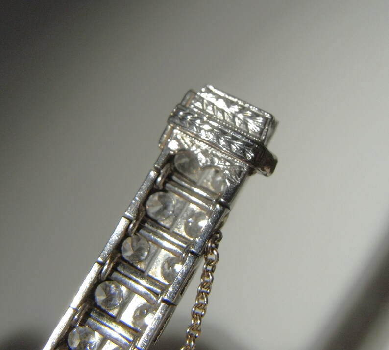 May include: A silver bracelet with a row of clear stones and an engraved clasp. The bracelet has a delicate chain attached to the clasp.