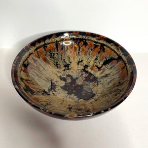 May include: A brown and black ceramic bowl with a speckled glaze. The bowl has a wide rim and a rounded bottom.