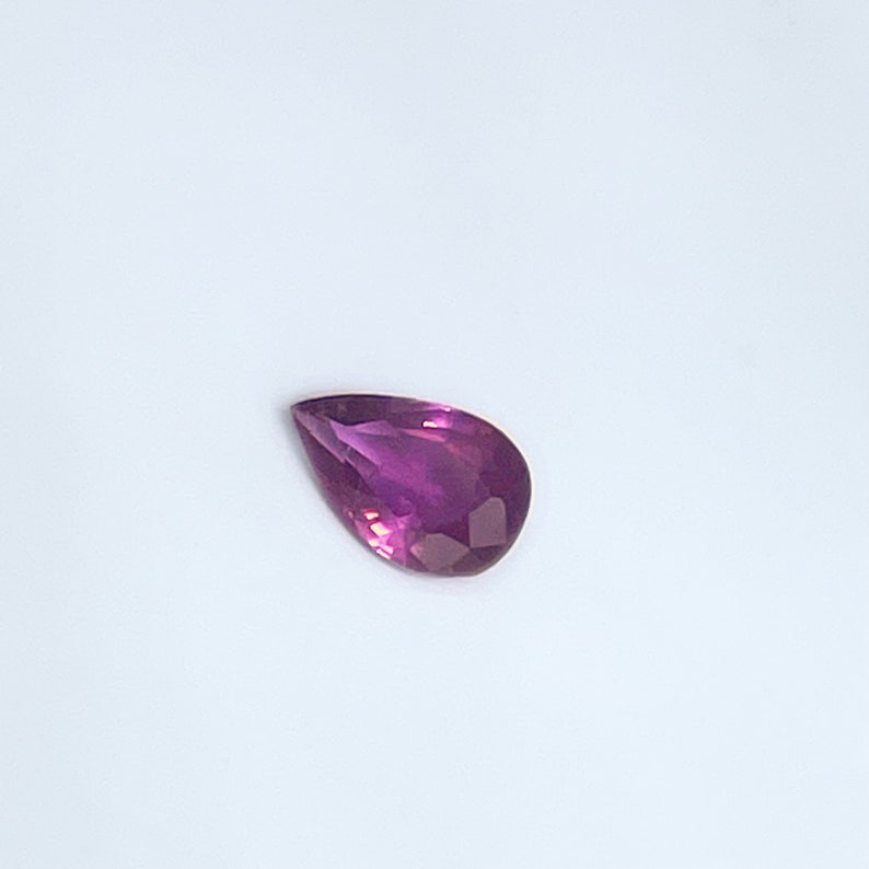 May include: A pear-shaped gemstone with a deep purple hue.