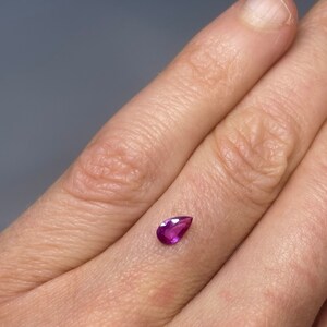 May include: A teardrop-shaped, deep pink gemstone with a faceted cut.
