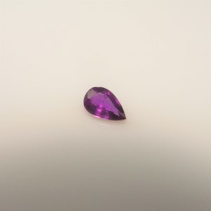 May include: A pear-shaped purple gemstone with a smooth, polished surface.