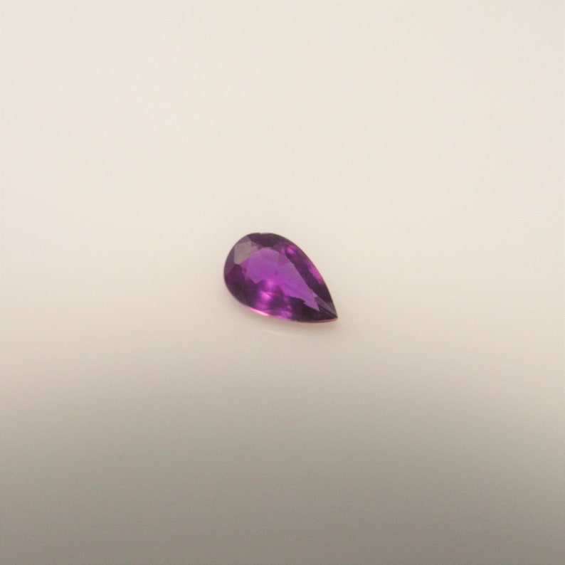 May include: A pear-shaped purple gemstone with a smooth, polished surface.
