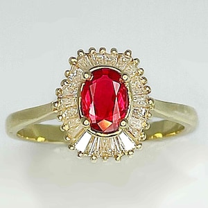 Puede incluir: Un anillo de oro con una piedra preciosa ovalada roja rodeada por un halo de piedras blancas más pequeñas.