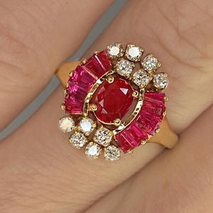Op de afbeelding: Een gouden ring met een grote rode robijn omringd door kleinere rode robijnen en diamanten.