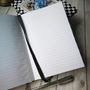 May include: Open lined journal with a black ribbon bookmark and a silver pen with the word "etsy.com" printed on it. The journal has a black and white checkered cover with a picture of a woman in a blue dress.