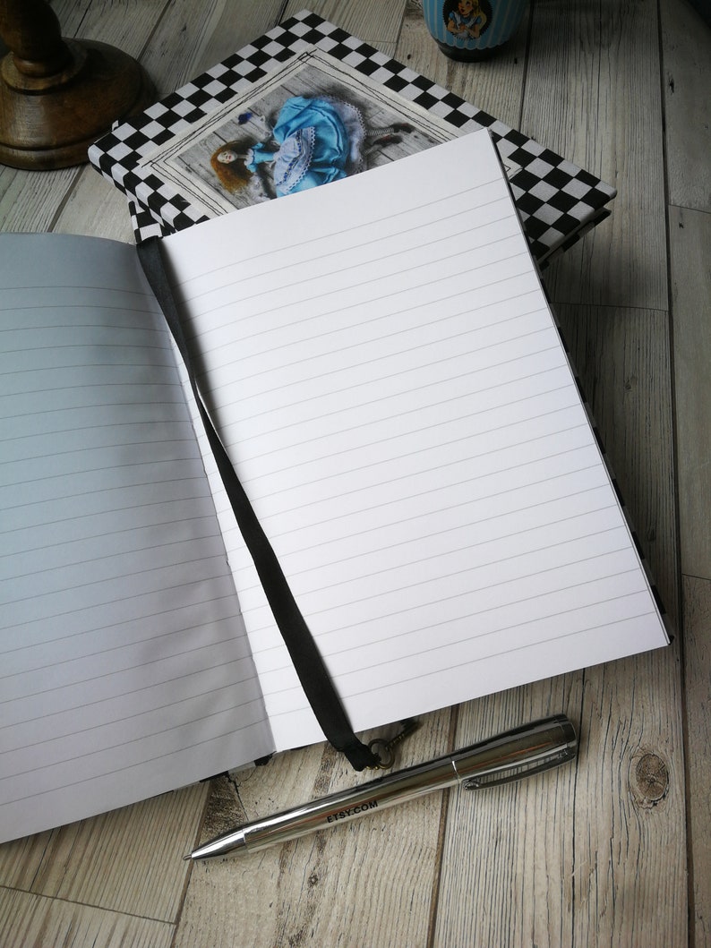 May include: Open lined journal with a black ribbon bookmark and a silver pen with the word "etsy.com" printed on it. The journal has a black and white checkered cover with a picture of a woman in a blue dress.