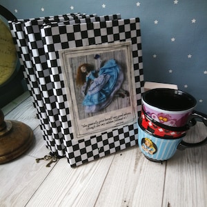 May include: Three black and white checkered notebooks with a quote from Alice in Wonderland on the front cover. The quote reads "She generally gave herself very good advice, (though she very seldom followed it)." The notebooks are stacked on top of each other and have a key attached to the spine.