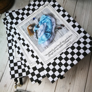 May include: Three black and white checkered notebooks with a quote from Lewis Carroll's Alice in Wonderland. The quote reads "She generally gave herself very good advice, (though she very seldom followed it)."  The notebooks feature a photo of a doll dressed as Alice falling down a rabbit hole.