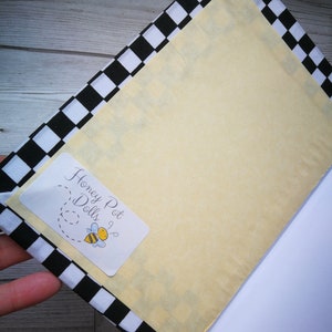 May include: A black and white checkered notebook with a yellow cover. The cover has a sticker with the text "Honey Pot Dolls" and a cartoon bee.