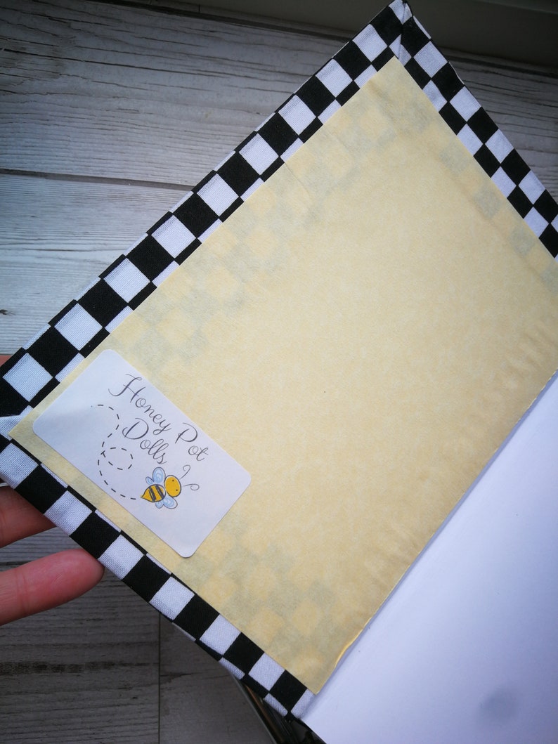 May include: A black and white checkered notebook with a yellow cover. The cover has a sticker with the text "Honey Pot Dolls" and a cartoon bee.