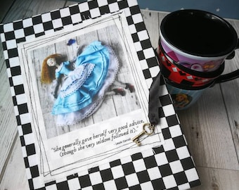 May include: A black and white chequered notebook with a quote from Lewis Carroll's Alice in Wonderland. The quote reads "She generally gave herself very good advice, (though she very seldom followed it)." The notebook features a picture of Alice falling down a rabbit hole.