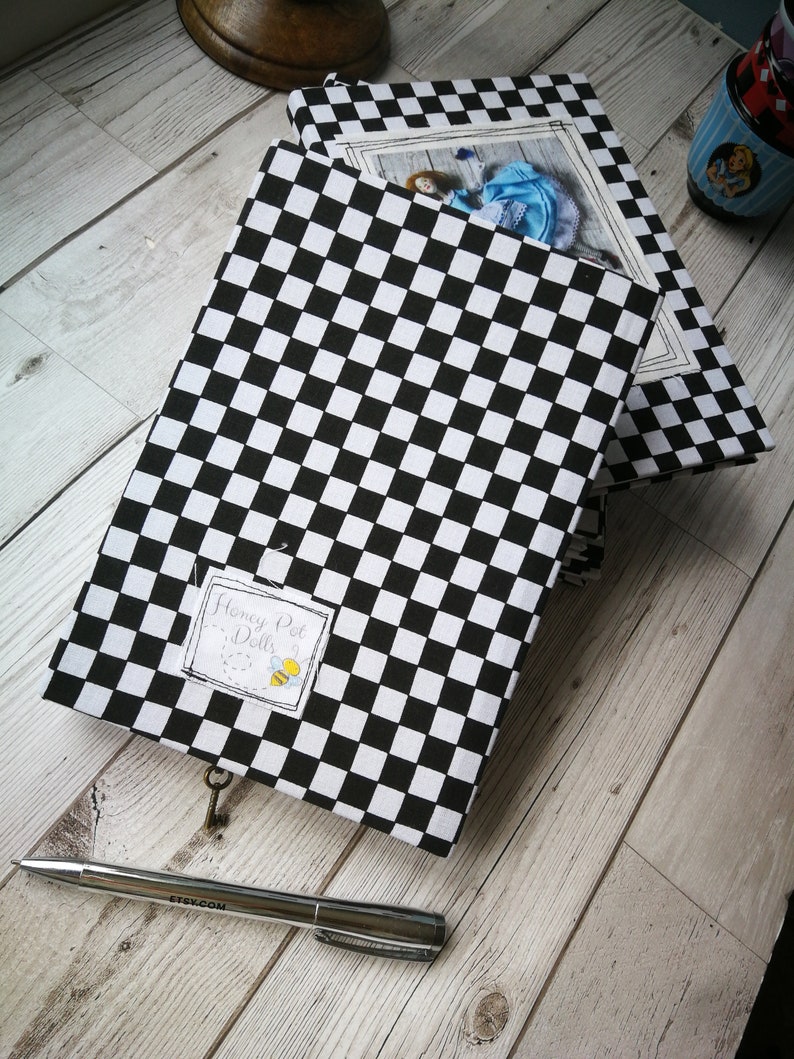 May include: Two black and white checkered notebooks with a keyhole and a label that says "Honey Pot Dolls". The top notebook has a photo of a doll wearing a blue dress.