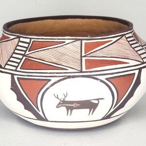 May include: A handcrafted, round ceramic pot with a wide opening. The pot features a white base with geometric patterns in brown and black. A deer silhouette with an arrow is centered on the pot's body. The interior is a warm brown colour.