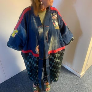 May include: A denim kimono-style jacket with red trim and patchwork details. The jacket features a mix of blue denim, patterned fabric, and graphic patches. The bottom portion has a green and black checkered pattern.