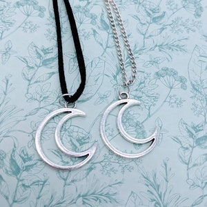 Può includere: Due collane con ciondolo a forma di mezzaluna d'argento, una su un cordoncino nero e l'altra su una catena d'argento.