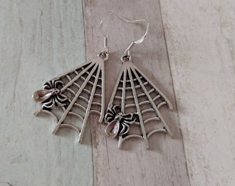 May include: A pair of silver spider web earrings with a spider detail. The earrings are dangling and have a web-like design.