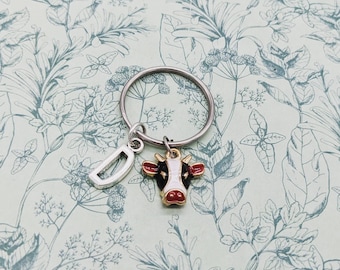 May include: A silver key chain with a black and white cow charm and a silver letter D charm.