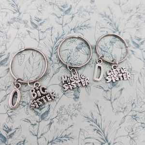 May include: Three silver keychains with charms that say "Big Sister", "Middle Sister", and "Little Sister".