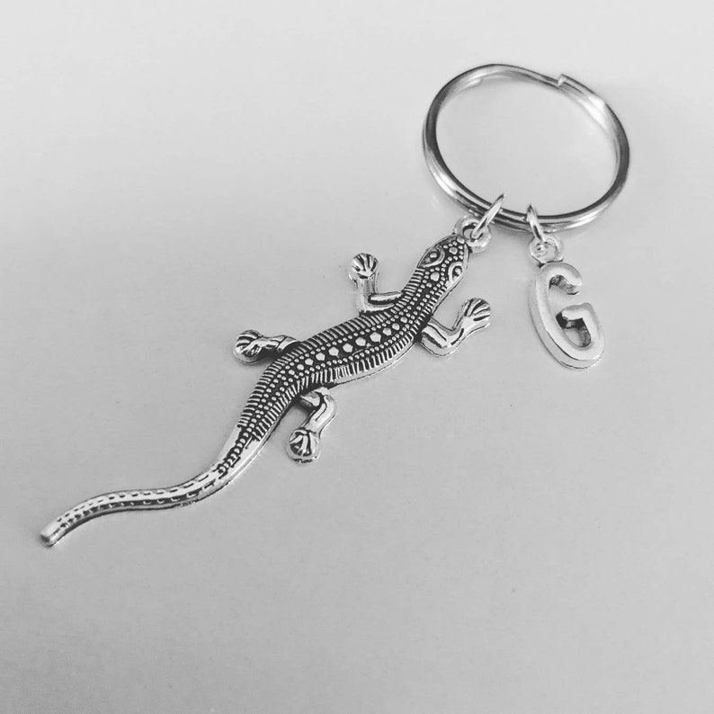 May include: Silver lizard keyring with a silver letter G charm attached to a silver key ring.