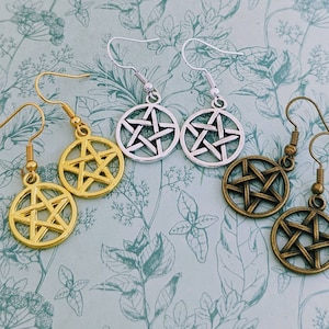 May include: A set of six silver and gold earrings featuring a pentacle design. The earrings are on a white background with green foliage.