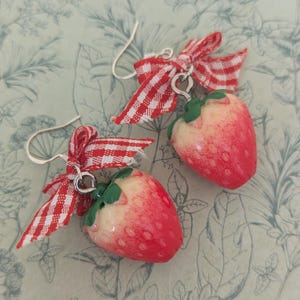 May include: A pair of red and white gingham ribbon dangle earrings with a red and white strawberry charm.