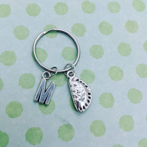 May include: Silver keyring with a letter M charm and a pie charm. The keyring is on a green polka dot background.