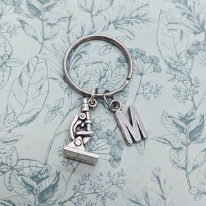 May include: Silver keyring with a microscope charm and a letter M charm. The charms are attached to a silver key ring.