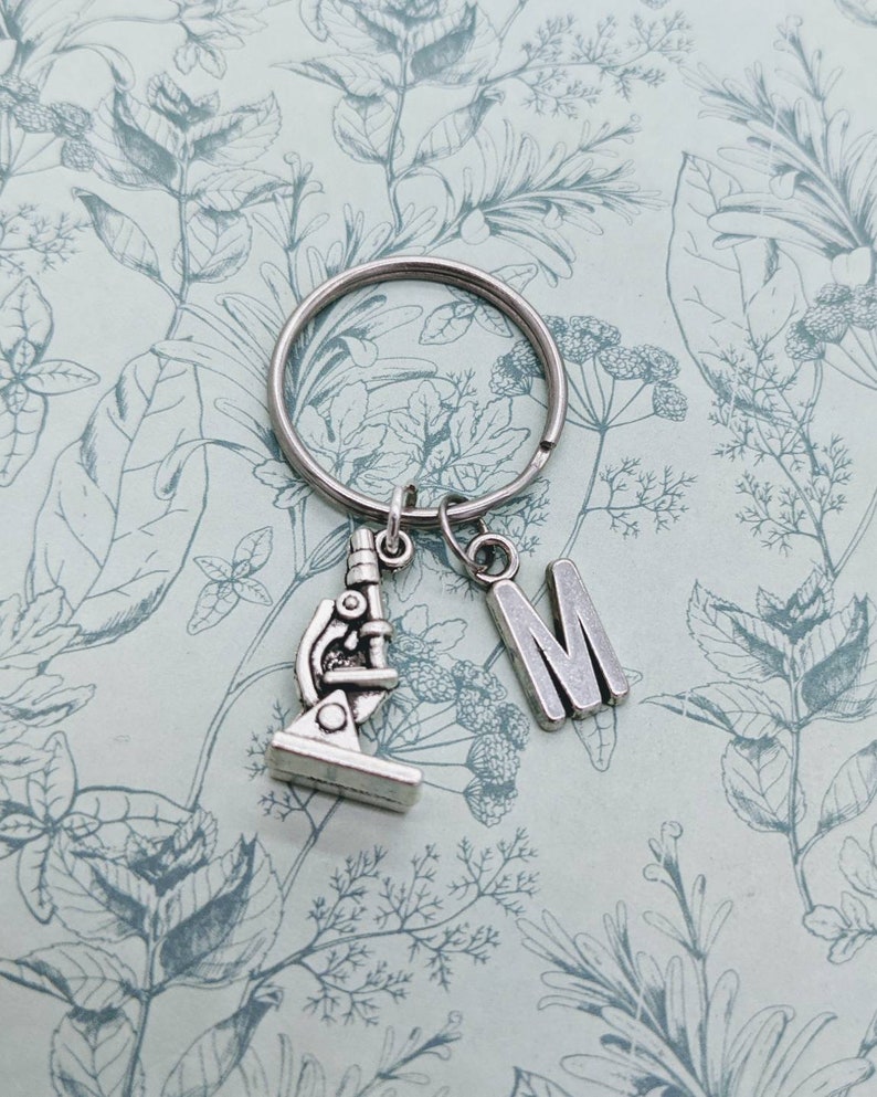 May include: Silver keyring with a microscope charm and a letter M charm. The charms are attached to a silver key ring.