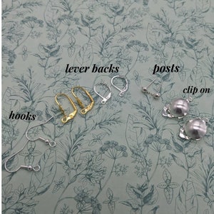 May include: A close-up of different earring findings, including lever backs, posts, hooks, and clip-on earrings. The findings are silver and gold toned.