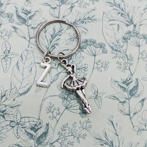 May include: Silver ballerina charm keyring with a letter Z charm. The charms are attached to a silver key ring. The charms are on a white background with a floral pattern.
