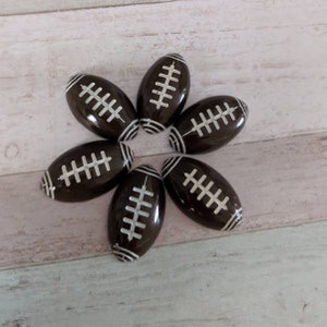 Puede incluir: Seis adornos de color marrón y blanco con forma de balón de fútbol con detalles de costura blancos.