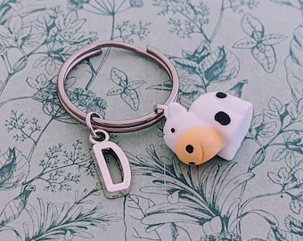 May include: A silver key chain with a black and white cow charm and a silver charm with the letter D.