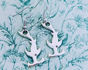 Pode incluir: Um par de brincos de prata em forma de chifres de veado estilizados. Os brincos estão sobre um fundo azul claro com um padrão floral.