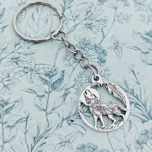 May include: Silver key chain with a wolf howling at the moon charm. The charm is surrounded by a feather design.