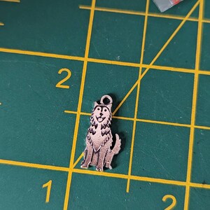 May include: A silver charm in the shape of a husky dog. The dog is sitting with its tongue sticking out and its ears perked up.