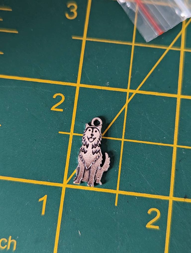 May include: A silver charm in the shape of a husky dog. The dog is sitting with its tongue sticking out and its ears perked up.