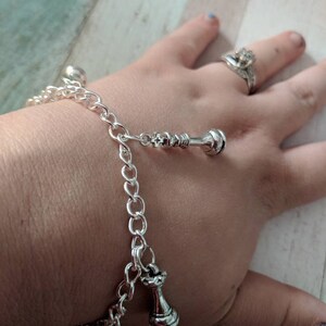May include: A silver chain bracelet with three silver chess piece charms. The charms are a king, a queen, and a pawn.