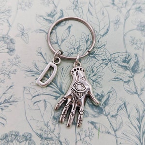 May include: Silver charm keychain with a letter D charm and a silver hand charm with an eye design.