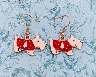May include: A pair of dog-shaped earrings with copper-colored hooks. Each earring features a light tan dog wearing a red sweater with a white Christmas tree design. The earrings are set against a light blue background.