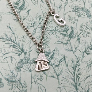 May include: A silver necklace with a charm of a small house and a charm of the letter G.