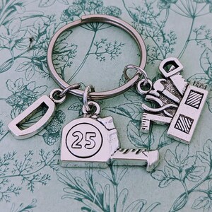 May include: Silver keychain with a measuring tape charm that says "25", a letter "D" charm, and a charm of a toolbox with tools.