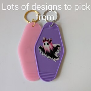Può includere: Due portachiavi, uno rosa e uno viola. Il portachiavi viola ha un fantasma con un fiocco rosa e dettagli in bianco e nero. I portachiavi hanno la forma di chiavi di camera d'albergo.