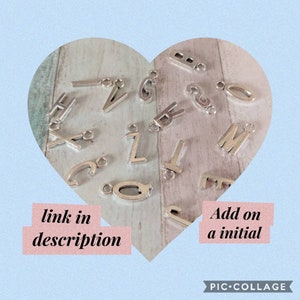May include: A collection of silver letter charms in a heart-shaped frame. The charms are arranged randomly and include letters A through Z. The text "link in description" and "Add on a initial" are visible below the charms.