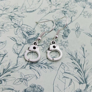 May include: A pair of silver dangle earrings featuring a handcuff design. The earrings have a simple, minimalist style.