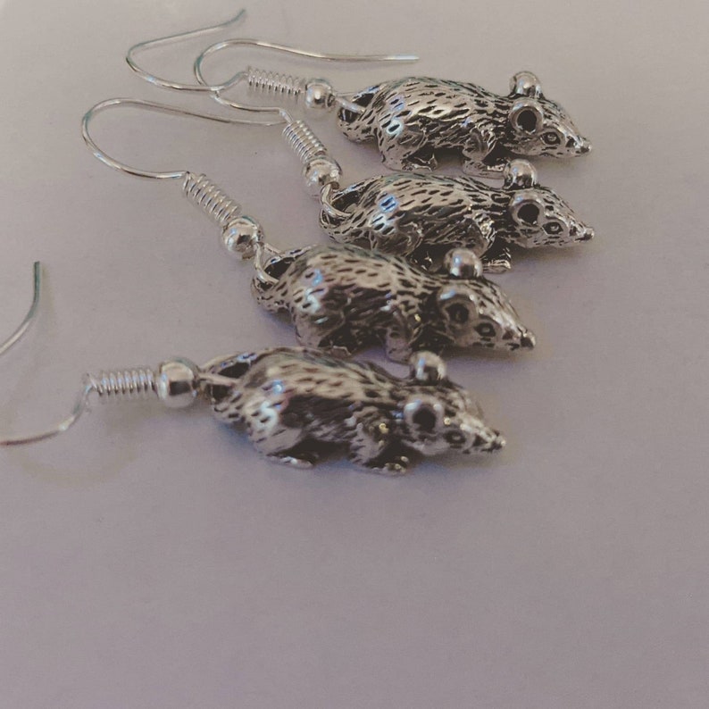 May include: Four pairs of silver rat earrings. Each earring features a detailed rat charm hanging from a silver hook.
