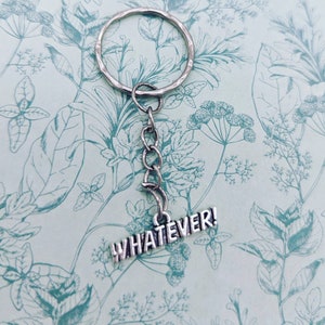 May include: Silver keychain with a silver ring and a silver chain attached to a silver charm that says "WHATEVER!" The keychain is on a light blue background with a floral pattern.