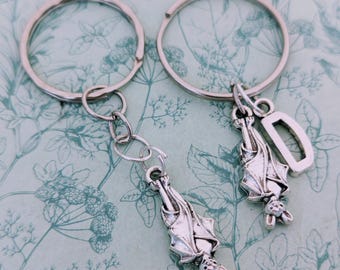 May include: Two silver keychains with bat charms. One bat charm has a letter D attached to it.